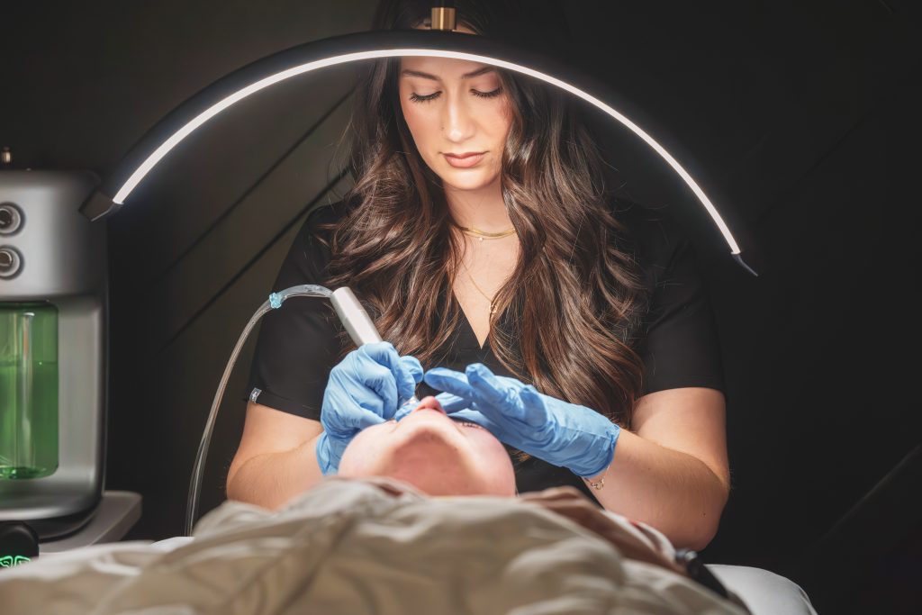 esthetician performing a laser treatment on a patient.